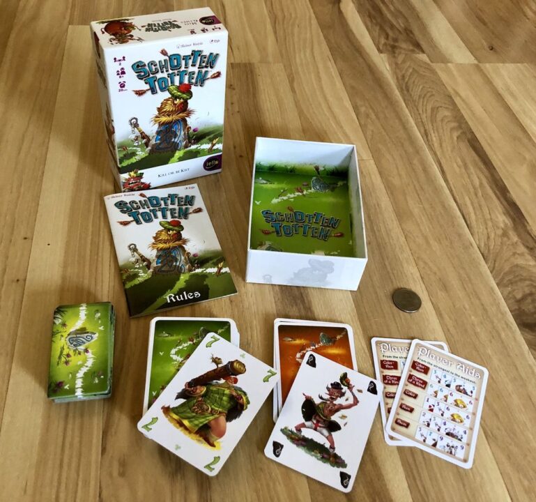 Schotten Totten - Components, unboxed, with a quarter for scale. From left to right in the foreground: 9 "stone" tiles; clan cards; tactics cards; and two player aids. - Credit: c_mcc