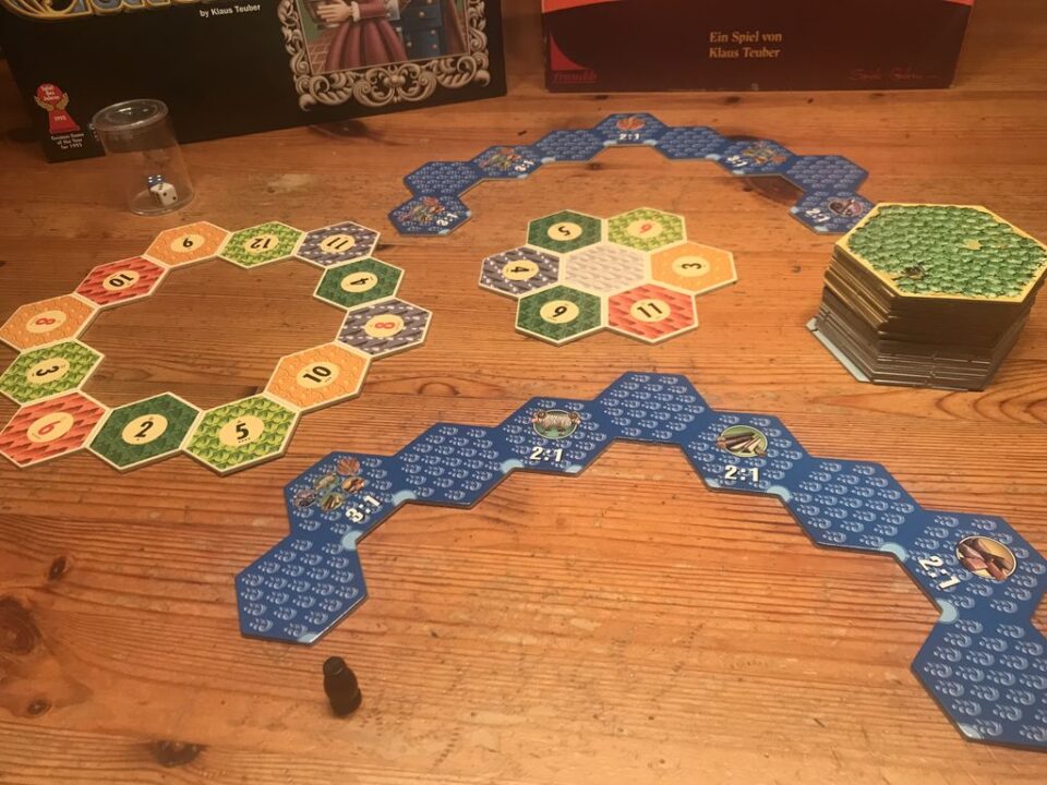 CATAN - The (old) German ed has the well known tiles (see pile at right). The Japanese ed (2002) has 4 gameboard parts, which can be arranged in several ways. - Credit: Reinhard Sabel